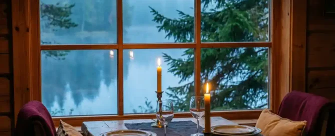 Romantisch gedekte tafel voor twee bij kaarslicht met kristallen wijnglazen, rustiek houten interieur en mistig bosmeer in de schemering.