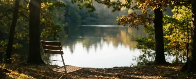 Houten terras met verweerde bistrostoel bij een spiegelgladde vijver, omgeven door gouden herfsteiken op de Veluwe in het avondlicht.