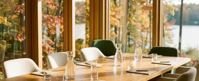 Vergaderzaal met vloer-tot-plafond ramen met uitzicht op het Veluwse bos en meer, houten tafel met waterkaraffen en notitieblokken, gouden herfstlicht.