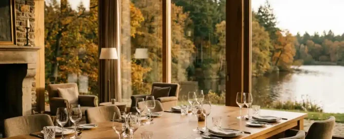 Rustieke vergaderzaal met eiken tafel en glaswerk, omgeven door herfstbos en meer in de Veluwe, gouden middaglicht.