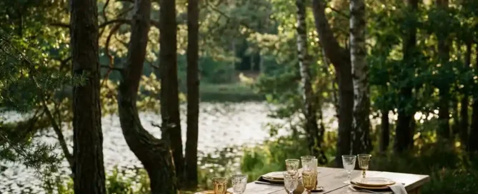 Rustieke eiken eettafel met elegant glaswerk aan de bosrand van de Veluwe, gouden middaglicht door dennenbomen en een kalm meer op de achtergrond.