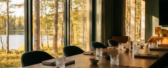 Vergadertafel van eiken met glaswerk en leren notitieboeken, met uitzicht op Veluwse bossen en meer in herfstig ochtendlicht.